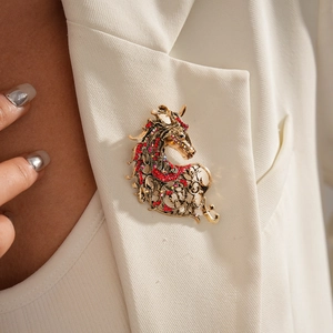 Detail view of a vintage gold horse head brooch with red rhinestones on a white blazer