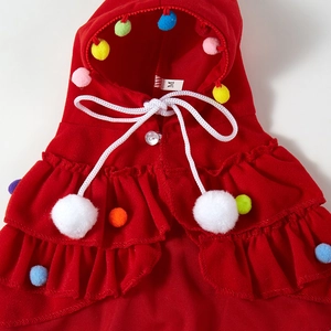 Detail of red Christmas pet cloak with size M label, colorful pom poms and soft texture