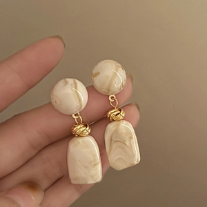 Detail of vintage marble resin earrings with golden knot accents and beige geometric drop