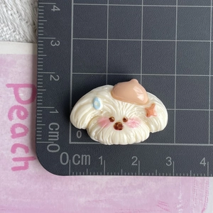 Close-up of a 3cm white dog resin charm with a beige beret measured on a black ruler