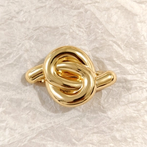Elegant gold metal twisted knot hair clip accessory on textured paper background