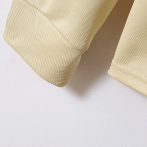Close-up of light yellow waffle knit fabric texture and stitching details on a polo shirt