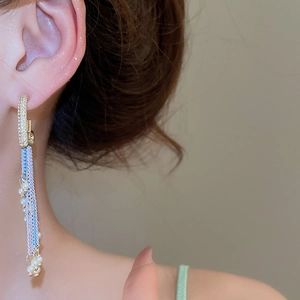 Close-up of heart-shaped pearl chain fringe earrings worn on the ear in gold finish