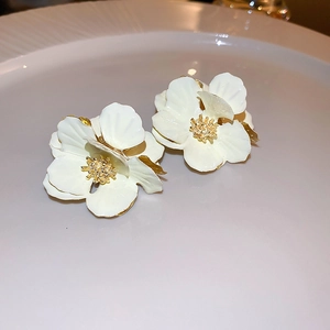 Close-up of elegant white layered flower earrings with golden stamen on ceramic plate
