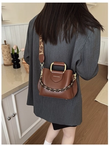 Detail of a brown leather bucket bag with gold metal handle and logo lettering