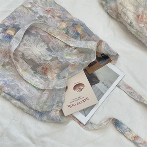 Detail showing translucent floral lace fabric with feather-like texture on a blue tote bag