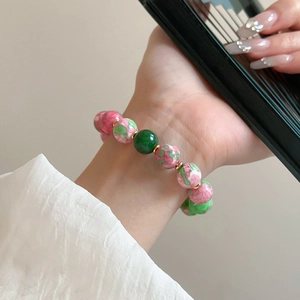 Detail of pink floral ceramic beads and green pearls on an elastic gold plated bracelet