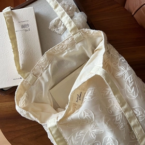 Detailed close-up of intricate lace floral embroidery on a vintage cream cotton tote bag