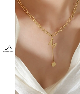 Detail of gold stainless steel necklace with M letter pendant on a female model neck