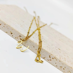 Détail des pendentifs lettres W et B plaqués or 18k en acier avec accents de cœur