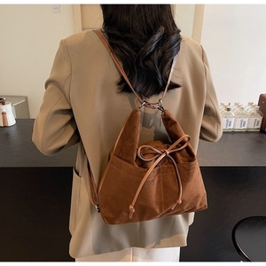 Brown suede drawstring backpack shown on model wearing a khaki blazer in a soft indoor setting