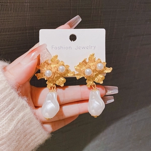 Boucles d'oreilles fleur dorée avec perles baroques sur carte blanche portées à la main