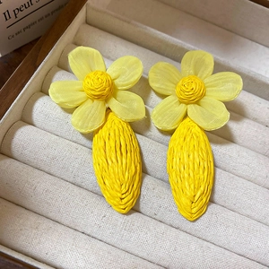 Detailed macro view of yellow flower tassel earrings with woven teardrop pendants in a box