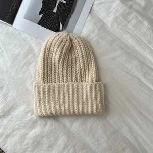 Close-up of beige chunky knit beanie texture on white fabric with fashion magazine