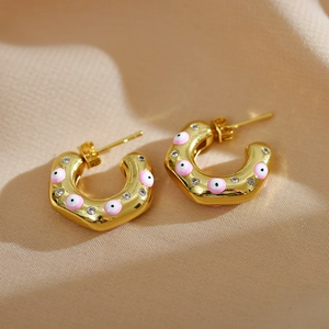 Macro view of C-shape gold earrings with pink enamel evil eye and sparkling crystals