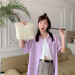 Close-up of white bubble textured cosmetic bag with brand label held by a female model