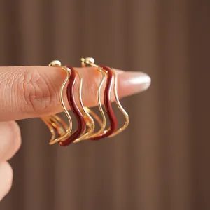 Irregular wavy gold earrings with dark red enamel finish on fingers, minimalist style