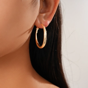 Close-up of a model wearing a polished golden geometric C-shaped hoop earring