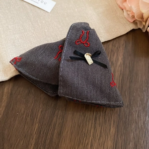 Detail of grey denim hair clip with red embroidered bows and handmade gold tag