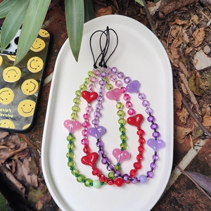 Colorful beaded heart phone straps in red, pink, and purple on a white ceramic tray
