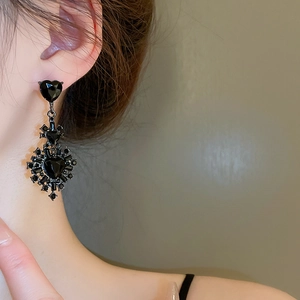 Detail of a vintage gothic black heart drop earring with intricate crystal embellishments