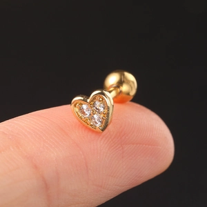 Close-up of golden heart earring with three zircons on fingertip showing actual size