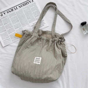 Detail of grey-green pleated tote bag with drawstring closure on minimalist background