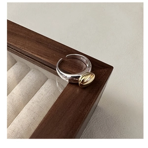 Detail of S925 sterling silver open ring in gold and silver tones on a wooden jewelry box