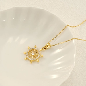 Golden ship rudder necklace with white zircon pendant on a sea shell background