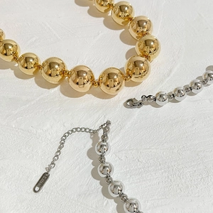 Exaggerated 18K gold and silver stainless steel beaded necklaces set on white texture