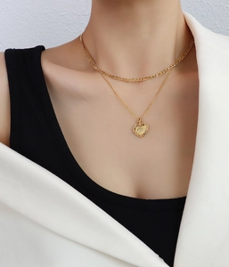 Gros plan d'un collier double rang doré avec pendentif cœur et chaîne Figaro sur mannequin