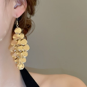 Close-up of a model wearing layered gold disc drop earrings with a metallic mirror finish