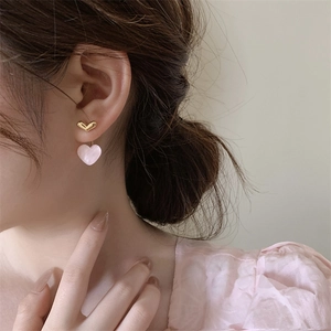 Detail of pink heart-shaped earrings with gold V-stud worn by a model in soft lighting