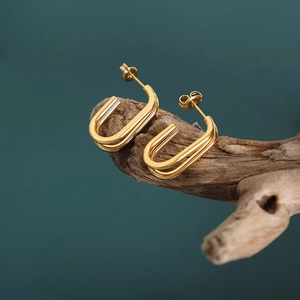 Elegant gold U-shaped geometric earrings displayed on natural wood with dark background
