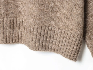 Gros plan détaillé de l'ourlet du pull en maille marron montrant la texture côtelée de qualité