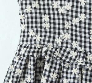Detailed close-up of black and white plaid fabric with delicate white floral embroidery