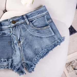 Detail der hellblauen Denim-Shorts mit ausgefransten Säumen und klassischem Metallknopf