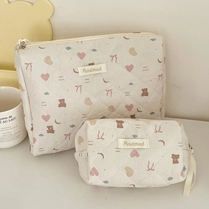 Dettaglio di pochette trapuntate beige con motivi di orsi e loghi ricamati