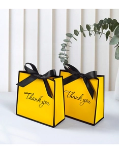 Detailed view of yellow paper gift bags with black ribbon bows and Thank You text