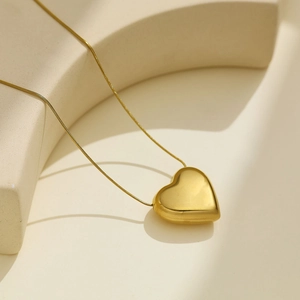 Gros plan d'un pendentif coeur doré sur une fine chaîne en métal au style minimaliste