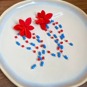Handmade red flower earrings with colorful bead tassels on a ceramic plate
