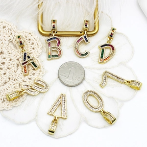 Pendentifs alphabet en zircon coloré plaqués or 18k présentés avec une pièce de monnaie