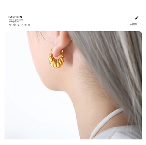 Close-up of gold croissant twist hoop earrings worn on ear with textured spiral pattern