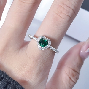 Close-up of elegant heart-shaped emerald green gemstone ring with halo diamond setting