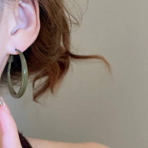Close-up of a model wearing dark green enamel geometric hoop earrings in a minimalist style