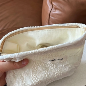 Detail of white lace makeup bag with simple wish label and top zipper closure