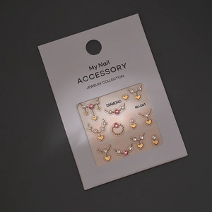 Macro shot of gold heart and pink crystal nail art charms on a white display card