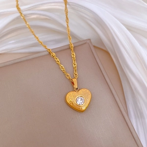 Detail of gold heart pendant with crystal on rope chain against white silk fabric