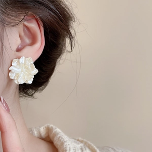 Close-up of a cream floral stud earring with pearl luster on a female model's ear