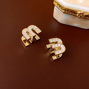 Macro detail of gold M-letter earrings with pave zircon crystals on brown leather
